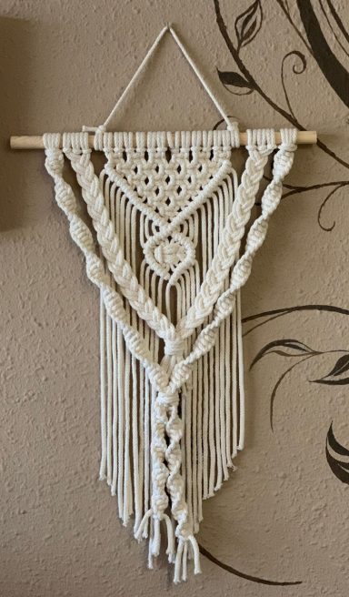 Decoración de pared en macramé blanco con patrones geométricos y flecos.